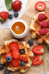 Delicious Belgian waffles with fresh berries and honey on white marble table, flat lay