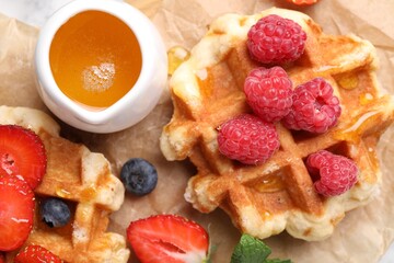 Delicious Belgian waffles with fresh berries and honey on parchment paper, top view
