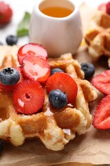 Delicious Belgian waffle with fresh berries and honey on parchment paper, closeup