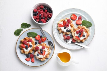 Delicious Belgian waffles with whipped cream and berries served on white table, flat lay