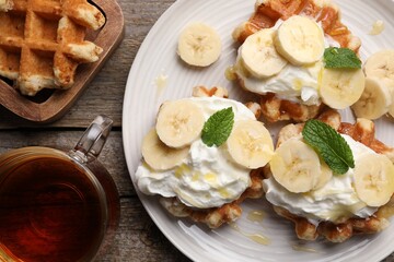 Obraz na płótnie Canvas Delicious Belgian waffles with banana and whipped cream served on wooden table, flat lay