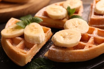 Tasty Belgian waffles with banana and mint on slate plate, closeup