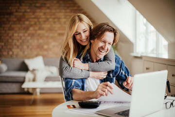 Happy young couple going over financials together at home - obrazy, fototapety, plakaty
