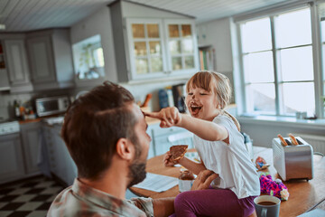 Young father and daughter having breakfast together and being messy in the kitchen - obrazy, fototapety, plakaty