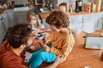 Young father and son being messy with chocolate spread in the kitchen at home - Powered by Adobe