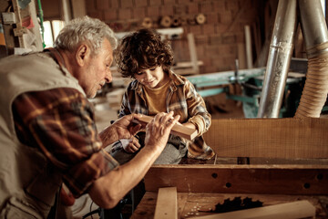 Fototapeta premium Young boy learning how to measure wood from his grandfather carpenter in the wood shop