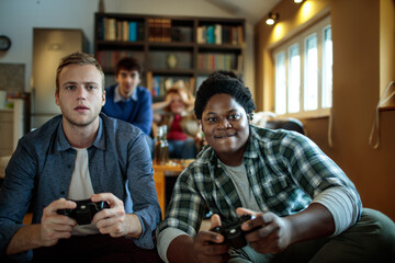 Two diverse male friends playing video games with a controller in the living room at home