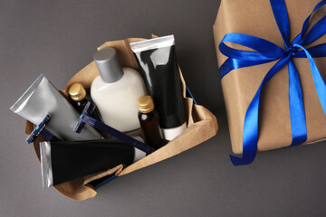 Gift box with different men's shaving accessories and cosmetics on dark grey background, flat lay