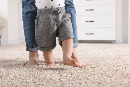 Mother supporting her baby son while he learning to walk on carpet at home, closeup. Space for text