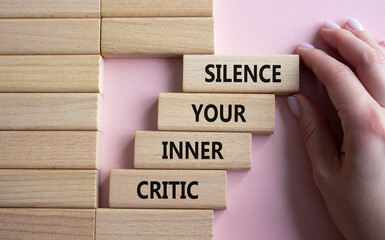Silence your inner critic symbol. Wooden blocks with words Silence your inner critic. Beautiful pink background. Businessman hand. Business and Silence your inner critic concept. Copy space. - obrazy, fototapety, plakaty