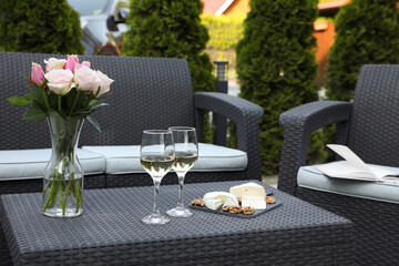Vase with roses, glasses of wine and food on rattan table on outdoor terrace