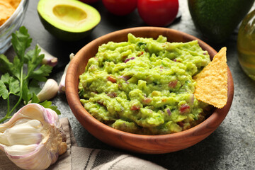 Delicious guacamole with nachos chips and ingredients on grey table, closeup