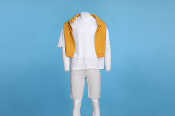 Male mannequin dressed in white t-shirt, stylish shorts and orange sweater on light blue background