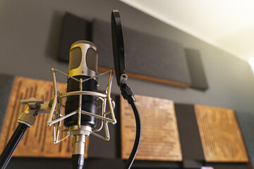 Condenser Microphone in Recording Studio - A close-up of a condenser microphone in a recording studio, with a shallow depth of field. In the blurred background, sound-absorbing panels can be discerned - obrazy, fototapety, plakaty
