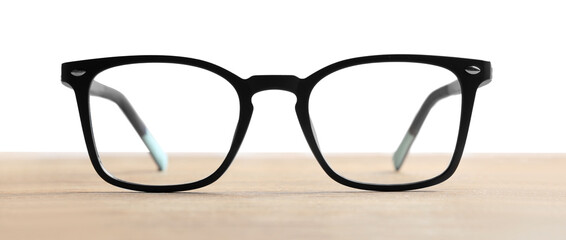 Stylish glasses with black frame on wooden table against white background