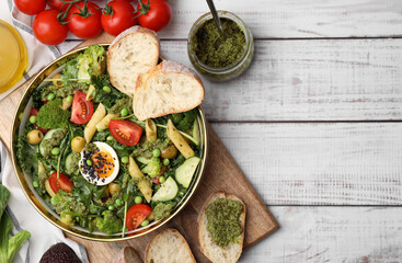 Delicious salad with pesto sauce in bowl and ingredients on white wooden table, flat lay. Space for text