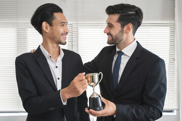 The hands of an employee receiving a golden cup reward from the company manager represent his...