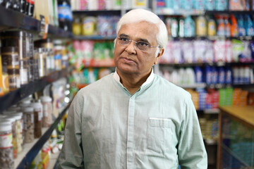 Old man standing in front of product shelf in grocery store. Confused old man buying grocery for home in supermarket. He is thinking and perplexed.