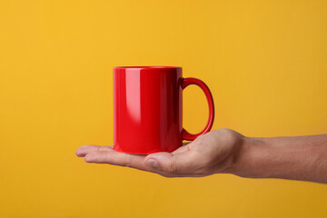 Man holding red mug on yellow background, closeup