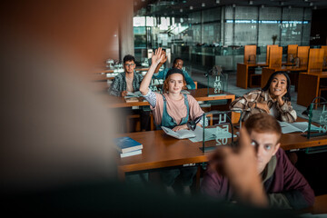 Young female student raising her hand in the college library