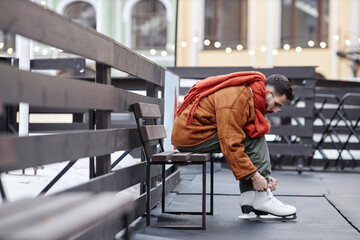 Side view portrait of man tying shoelaces on skates in ice skating rink outdoors, copy space - obrazy, fototapety, plakaty