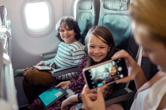 Young mother taking a picture of her kids on a smartphone while on their flight