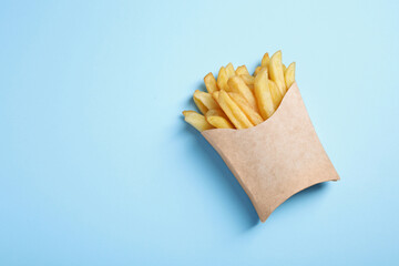 Paper cup with French fries on light blue table, top view. Space for text