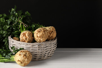 Fresh raw celery roots in wicker basket on white wooden table. Space for text