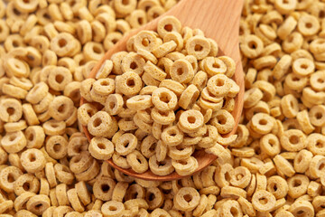 Dry oat flake rings in wooden spoonful. Pile of crispy round oatmeal cereals