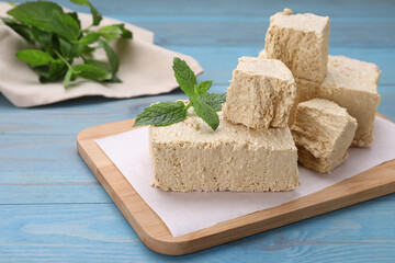 Pieces of tasty halva and mint on light blue wooden table, closeup. Space for text