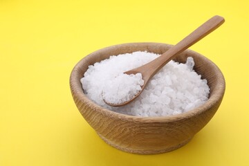 Bowl and spoon with sea salt on yellow background, closeup