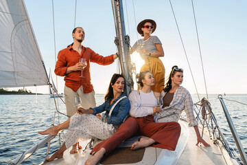 Group of happy friends drinking wine and relaxing on the sailboat during sailing in sea