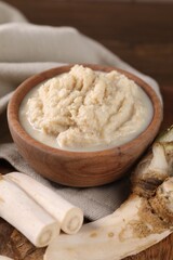 Spicy horseradish sauce in bowl and roots on table, closeup