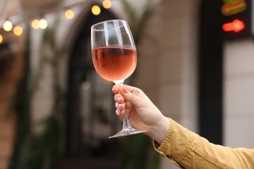 Woman holding glass of rose wine outdoors, closeup