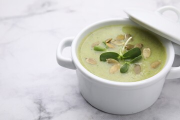 Delicious broccoli cream soup with pumpkin seeds on white marble table, closeup. Space for text