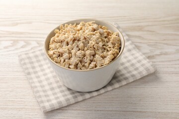 Tasty boiled oatmeal in bowl on light wooden table