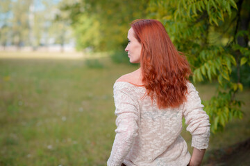 Fototapeta premium Relaxed redhead model with mesmerizing hazel eyes, posing gracefully while sitting in the park's tranquil fmbiance