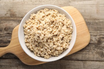 Tasty boiled oatmeal in bowl on wooden table, top view