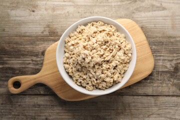 Tasty boiled oatmeal in bowl on wooden table, top view