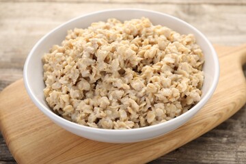 Tasty boiled oatmeal in bowl on wooden table, closeup
