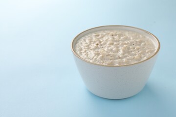 Tasty boiled oatmeal in bowl on light blue table, space for text