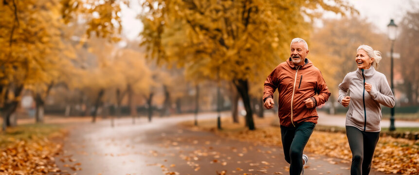 Senior couple running or jogging in a park in fall colors. Concept of health and fitness for mature or older people. Shallow field of view with copy space.	