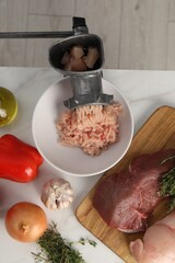Metal meat grinder with chicken mince and products on white marble table, flat lay