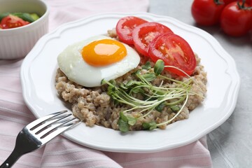 Delicious boiled oatmeal with fried egg, tomato and microgreens on table, closeup