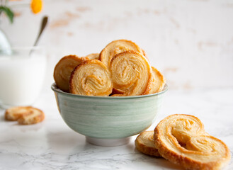 Puff pastry palmiers in a bowl on a white marble table. Homemade bakery for breakfast.