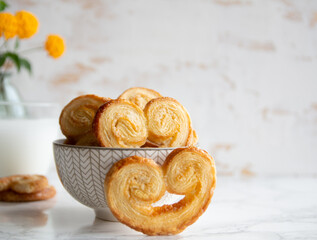Puff pastry palmiers in a bowl on a white marble table. Homemade bakery for breakfast.