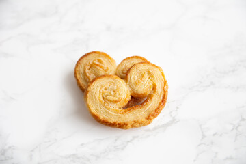 Two isolated Puff pastry palmiers on a white marble table.
