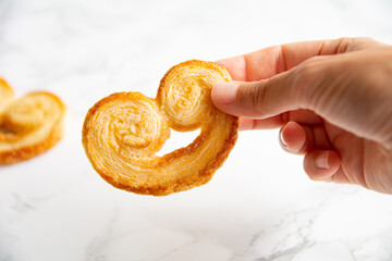Young woman's hand holding a puff pastry palmier on a light background. Homemade bakery.