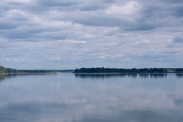 A peaceful, beautiful lake with calm water and a strip of forest visible in the distance on the other side. Harmony with nature