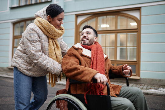 Portrait of smiling young woman assisting partner with disability outdoors in city streets